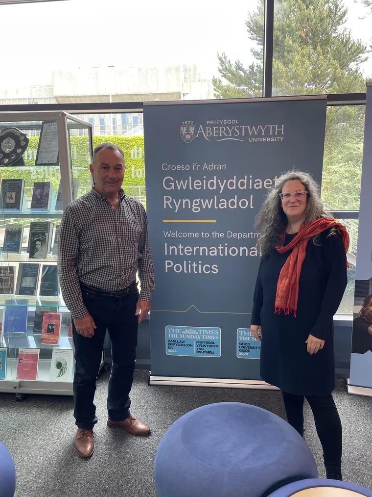 Huw Edwards and a colleague beside a banner for the Department of International Politics at Aberystwyth University.