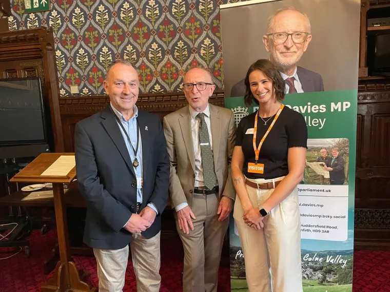 Huw Edwards with a researcher he has coached and a colleague at the Palace of Westminster, in front of an MP's banner.