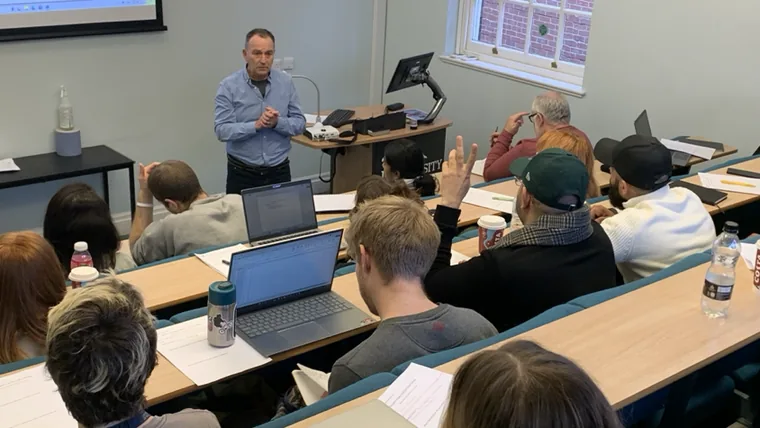 Huw Edwards presenting to researchers seated at laptops in a University of Hull teaching room.